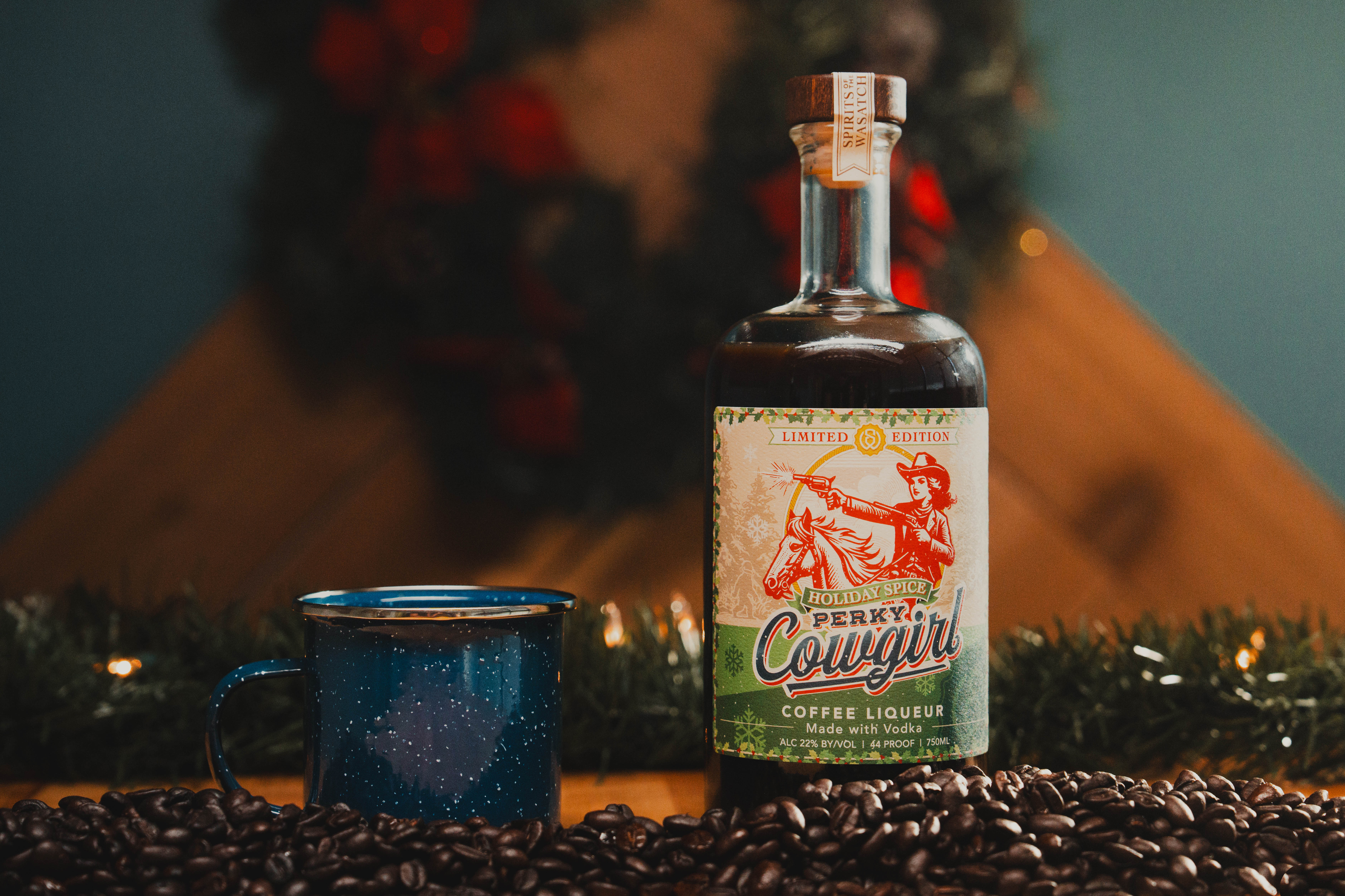 Perky Cowgirl Coffee Liqueur: Holiday Spice Bottle - Professionally photographed. Sitting atop an aging barrel with coffee beans.